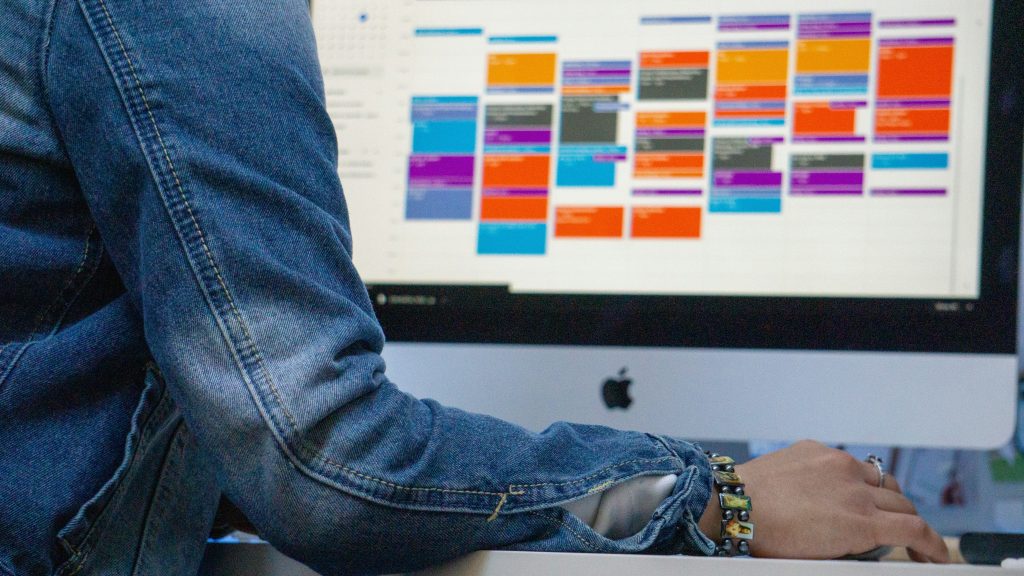 Colorful Schedule on a computer with person in blue denim jacket.