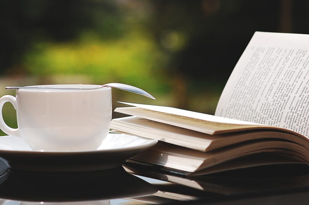 cup of tea on a saucer next to an open book outside